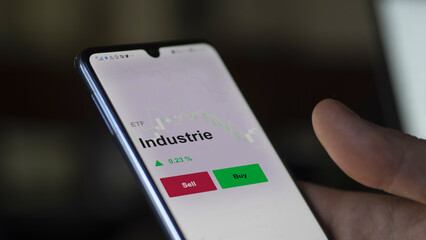 Un investisseur analyse un fonds etf industrie sur un graphique. Un téléphone affiche le cours de l'ETF Industrie