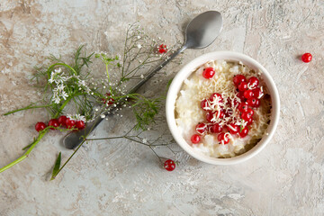 a bowl of rice porridge with white chocolate and red currants on a light table