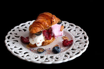 Small croissant Sandwich with ice cream and fruit on white plate and black background