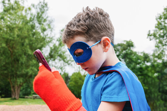 Little superhero using smartphone in park