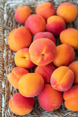 A large pile of ripe bright orange apricots lies close-up on a wicker plate.