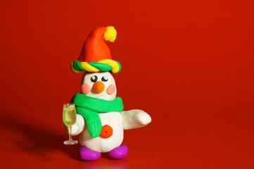 A small toy snowman with a glass of champagne in his hand on a red background. Festive mood.