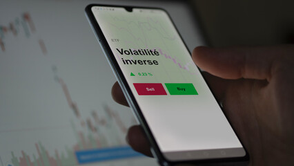 Un investisseur analyse un fonds etf volatilité inverse sur un graphique. Un téléphone affiche le cours de l'ETF. Texte en français francais Volatilité inverse