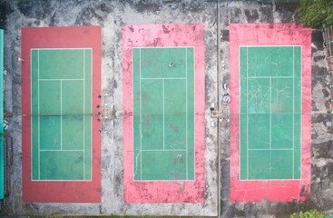 Aerial view of triple outdoor green and red hard tennis court with two players.