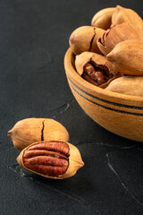 Part of a wooden bowl with in-shell pecans close-up on a dark concrete background