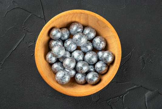Hazelnut candies in chocolate in a wooden bowl on a dark concrete background, top view