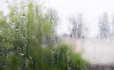 Heavy rain. Raindrops on the window glass on a summer day. Selective focus, shallow depth of field. Drops of water fall on a wet window. Glass full of drops during a downpour.