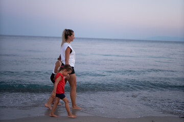 a young mother with two daughters enjoys an evening walk along the seashore. They are on vacation. Vacation concept.