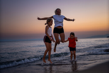 Fototapeta premium a young mother with two daughters enjoys an evening walk along the seashore. They are on vacation. Vacation concept.