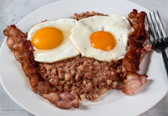 two fried eggs  on corn beef hash  with bacon