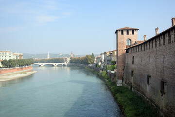A river near an ancient fortress wall with a tower and a bridge in the distance