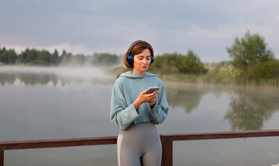 Portrait of beautiful fit woman wearing headphones and listening to music after jogging on the nature. Relaxation and resting concept