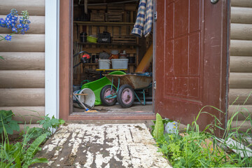a shed with an open door in which there is a household garden equipment - obrazy, fototapety, plakaty