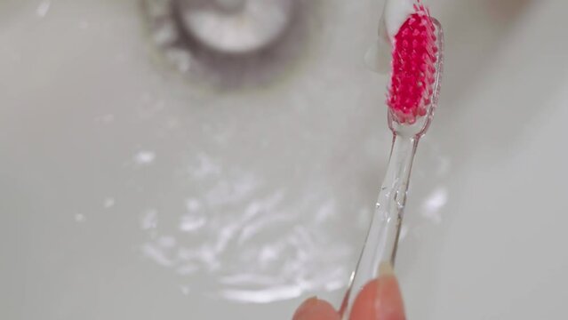 A close-up squeezes the white toothpaste onto the pink head of the toothbrush against the white shell.