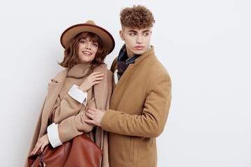 a happy couple in love is standing in beige stylish autumn coats on a white background and holding hands, a woman has a hat on her head and she is holding a bag in her hand