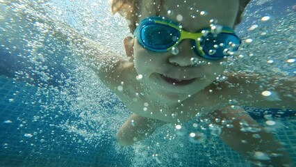 Male kid jumping to blue swimming pool bubbles water happy childhood underwater shot slow motion - Powered by Adobe