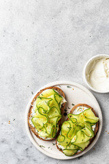 Cucumber sandwiches with soft cheese for healthy vegetarian breakfast on gray background. Top view with text space