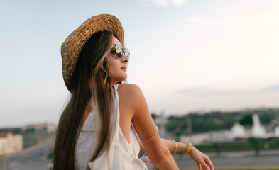 Portrait of a relaxed woman with hat looking forward at the horizon cityscape in the background copy space - 520256781