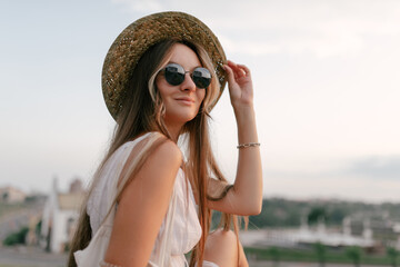 Portrait of a relaxed happy woman in white dress with hat looking at the camera. Cityscape in the background - 520256929