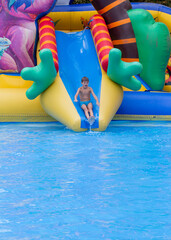 Boy has into pool after going down water slide during summer. little boy sliding down water slide and having fun