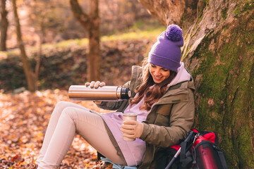 Woman taking a break pouring hot tea while mountaineering on an autumn day