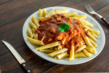 typical italian penne pasta on wooden background with tomato sauce