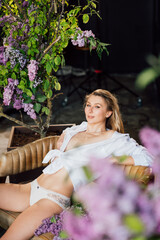 a blonde woman in a white shirt and panties on a leather chair with lilac 