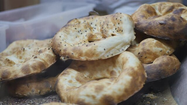 in a bakery, fresh hot baked rolls with sesame seeds fall into a pile, which the baker takes out of the tandoor with special metal hooks and throws into a pile