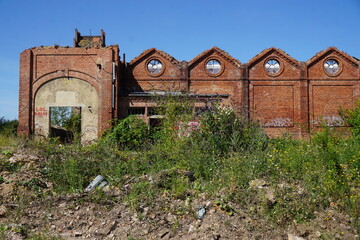 Alte rot-braune Backsteinfassade von verlassenem geschossenem Fabrikgebäude vor blauem Himmel bei...