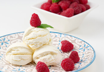 Vanilla ice cream balls with red raspberries in a round plate