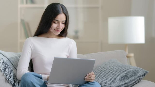 Confident arabian freelancer islamic young woman designer student sitting in comfort lotus pose on sofa working laptop browsing digital media pages studying online domestic education ecommerce concept