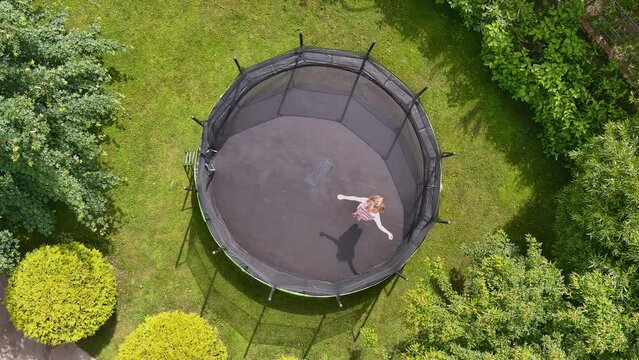 Aerial top-down view of a teenage girl jumping on trampoline in a backyard
