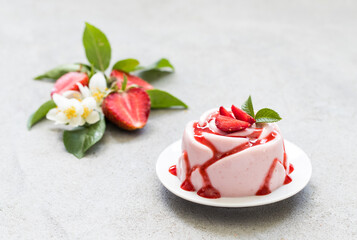 Strawberry Panna Cotta with sauce, in the shape of a rose, on a plate. Light grey background