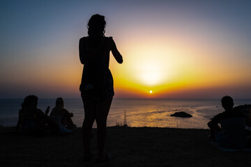 Woman enjoys the sunset on the shore of a paradisiacal beach during summer vacations.