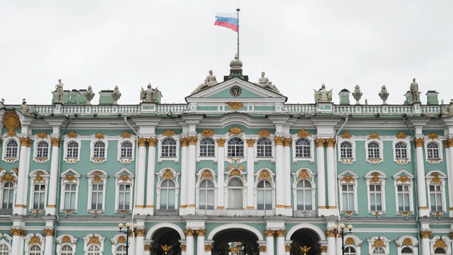 Facade of winter Palace with flag of Russia. Action. Greatest Russian architecture of Winter Palace in Saint Petersburg. Gold details and statues on turquoise facade of historic building in Russia