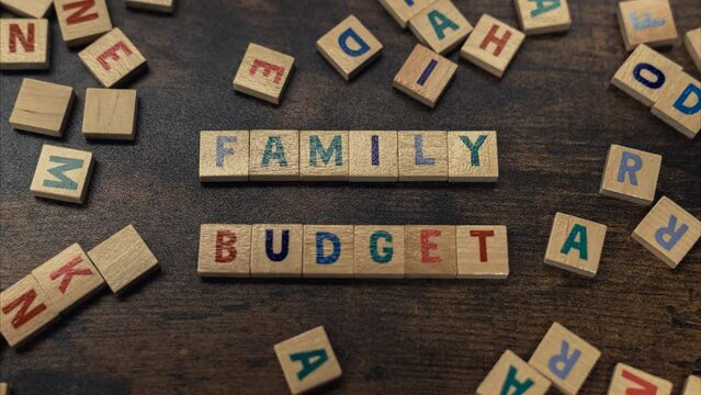 Scattered wooden colourful letters from a word game creating a slogan FAMILY BUDGET. Education about spending and saving money. High quality 4k footage