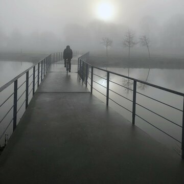 person cycling on the pier in the morning fog