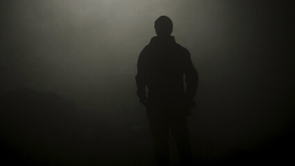 Black silhouette of man standing in smoky dark. Stock footage. Mysterious silhouette of young man stands in darkness lit only by dim light in haze