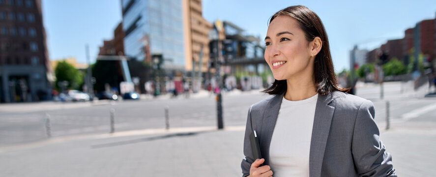 Young smiling proud successful Asian business woman, professional entrepreneur, office employee wears suit standing on city street looking in future career, thinking of success and leadership, banner.