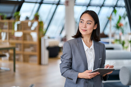 Young Asian business woman entrepreneur standing in office holding digital tablet. Businesswoman leader, professional company manager using smart corporate management technology looking at copy space.