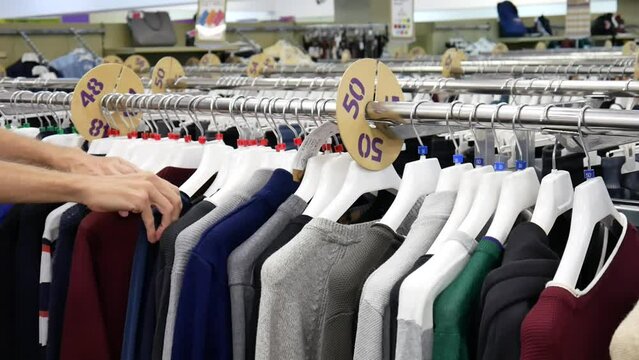 A row of pullovers on a clothing store rack and a male buyer chooses one