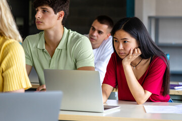 Asian female teen college student in class listening to lecture using laptop to take notes.