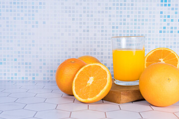 Glass of orange juice squeezed over a board and oranges around it.