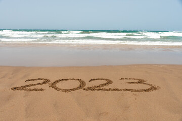 Fototapeta na wymiar Year 2023 written in the sand on the beach with the sea in the background