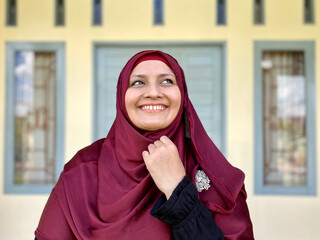 Asian woman wearing red hijab looking away in front of house