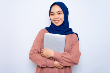 Fototapeta premium Smiling young Asian muslim woman in pink shirt holding laptop and looking at camera isolated over white background. People religious lifestyle concept
