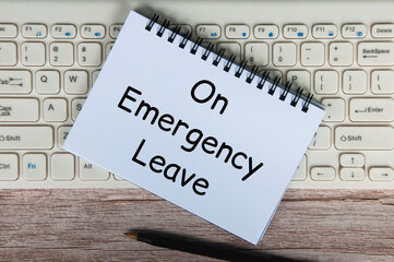 On emergency leave text on white notepad with pen and keyboard background.