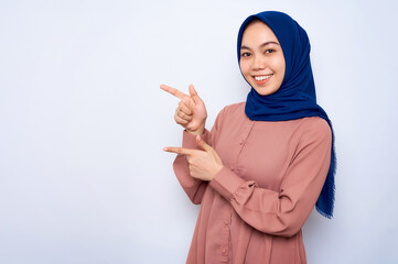 Cheerful young Asian muslim woman in pink shirt pointing fingers aside at copy space isolated over white background. People religious lifestyle concept