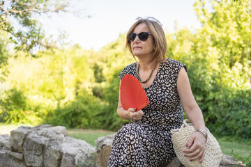 Senior woman sitting in a park and fanning herself on a hot summer day.