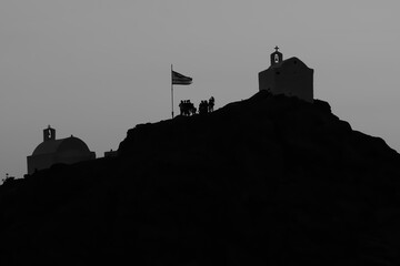 Tourists exploring the picturesque small chapels up the hill, next to the Greek national flag,  on...